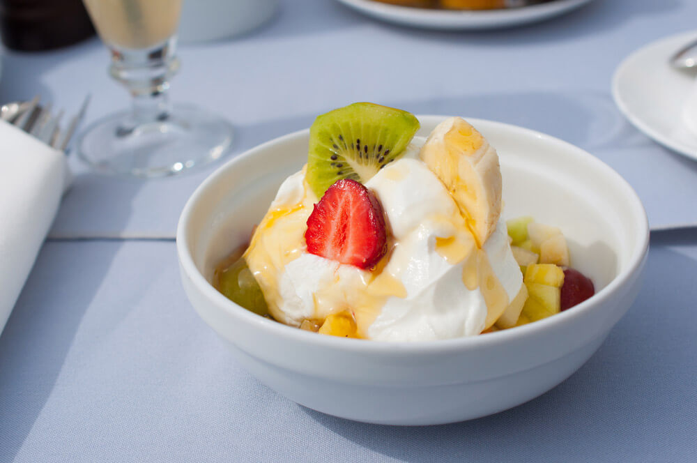 White bowl of yogurt topped with fresh fruit and drizzled with honey.