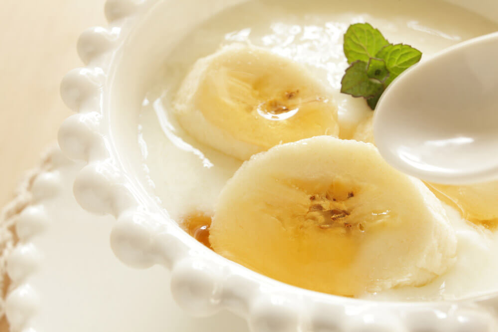 Close up photo of two slices of banana and fresh mint sitting on top of a white bowl of yogurt.