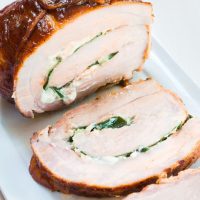 Top-angle view of a pork tenderloin that's been stuffed with goat cheese and spinach, tied and grilled over a white platter.