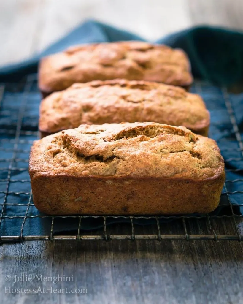 Three loaves of banana bread sitting horizontally on a cooling rack over a blue napkin. 