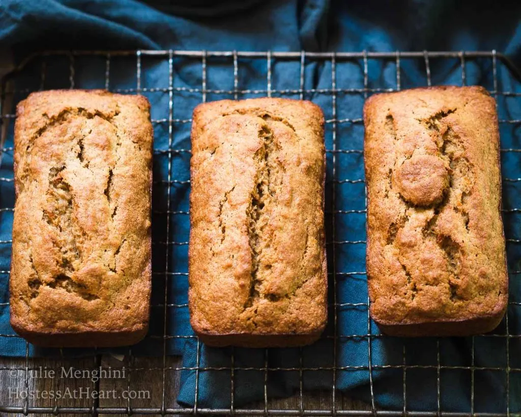 Top-down view of three loaves of banana bread with applesauce sitting on a cooling rack over a blue napkin.