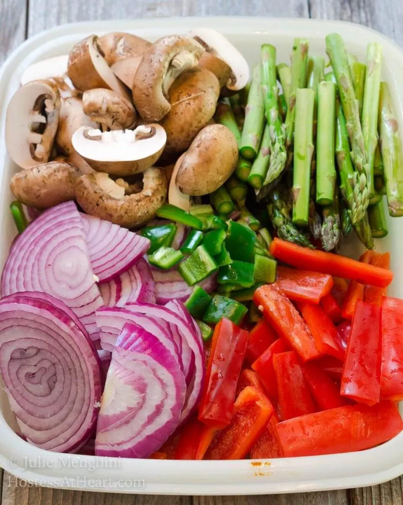 Ingredients used to make sheet pan Chicken Fajitas including red onion, mushrooms, asparagus, and red peppers.