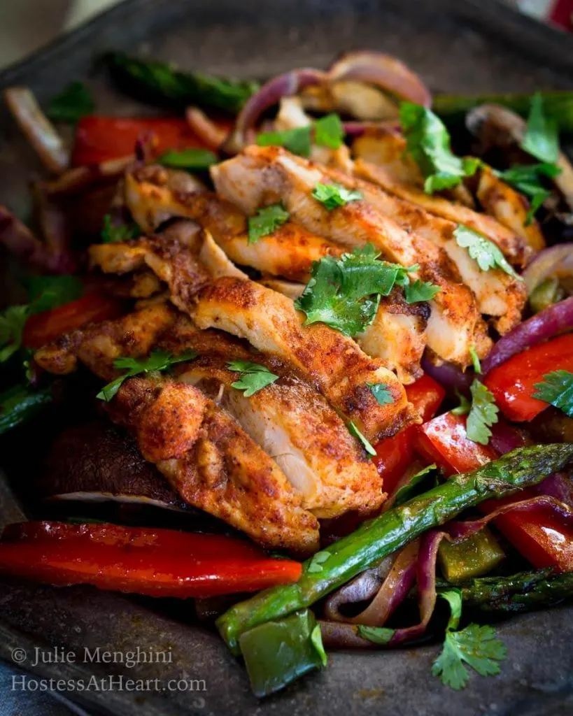 Close up view of Fajita vegetables topped with slices of chicken using the recipe for sheet pan chicken fajitas.