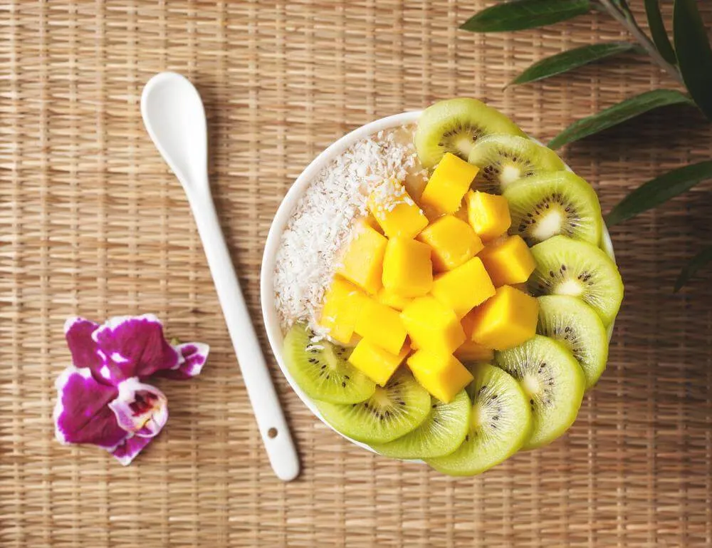 Top view of a bowl of diced mango and kiwi on a placemat next to a spoon