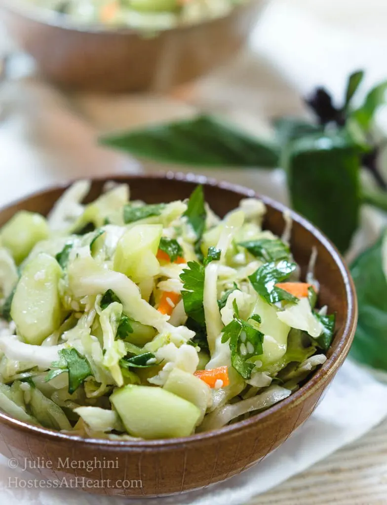 A wooden bowl heaped with Thai Basil Cabbage Slaw dotted with cucumbers and jalapenos.