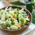 A wooden bowl heaped with Thai Basil Cabbage Slaw dotted with cucumbers and jalapenos.
