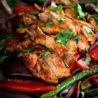 Close up view of Fajita vegetables topped with slices of chicken.