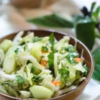 A wooden bowl heaped with Thai Basil Cabbage Slaw dotted with cucumbers and jalapenos.