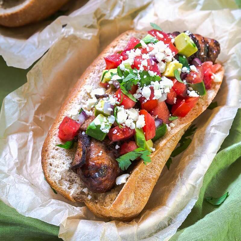 Top-down view of a Brat topped with Avocado Pico in a basket lined with parchment paper.