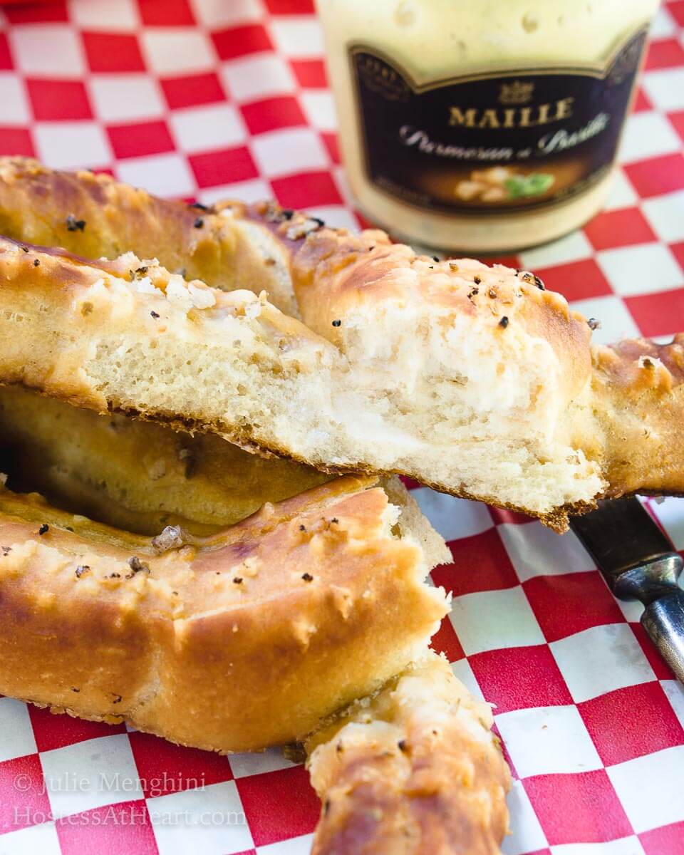 A torn open soft pretzel sits over a red checked paper napkin. A jar of mustard sits in the background.