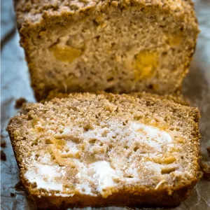 Top shot of a slice of peach bread shows cubes of yellow peaches and is covered in melted butter.