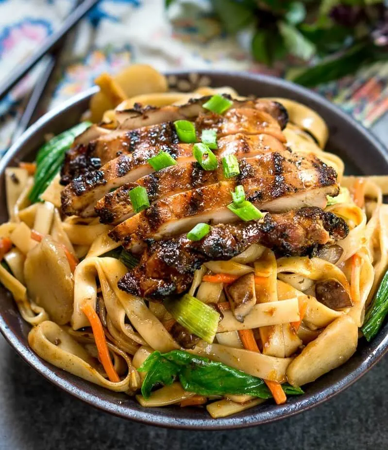 Bowl filled with Thai Basil Chicken Noodle recipe and garnished with Thai Basil. A set of chop sticks sit behind the bowl.