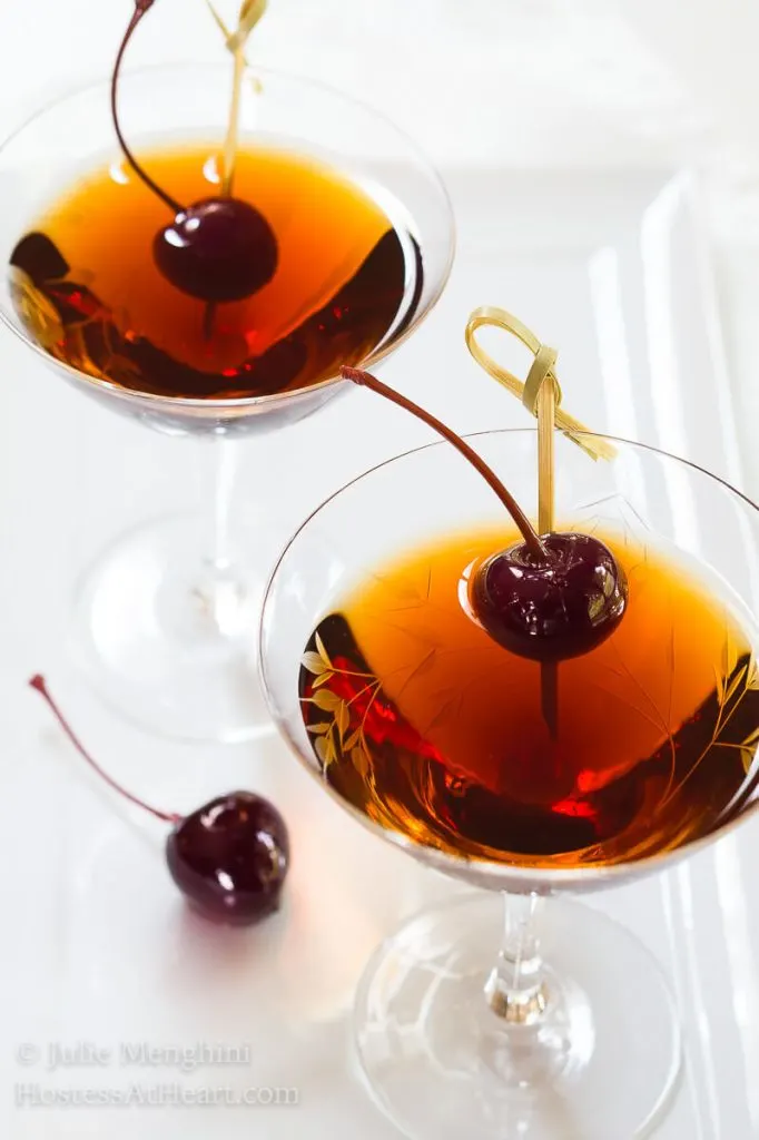 Top-down view of two martini glasses holding Cuban Manhattans. A Bada cherry sits next to the glass as well as one in the drink.