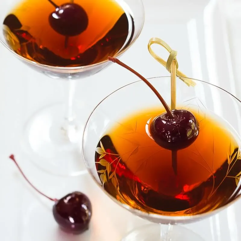 Cocktail glasses filled with a Cuban Manhattan cocktail and garnished with Bada cherries on bamboo skewers.