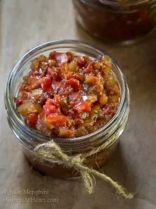 Top view of a jar of tomato onion chutney with a hemp string tied around it sitting on top of a wooden board.