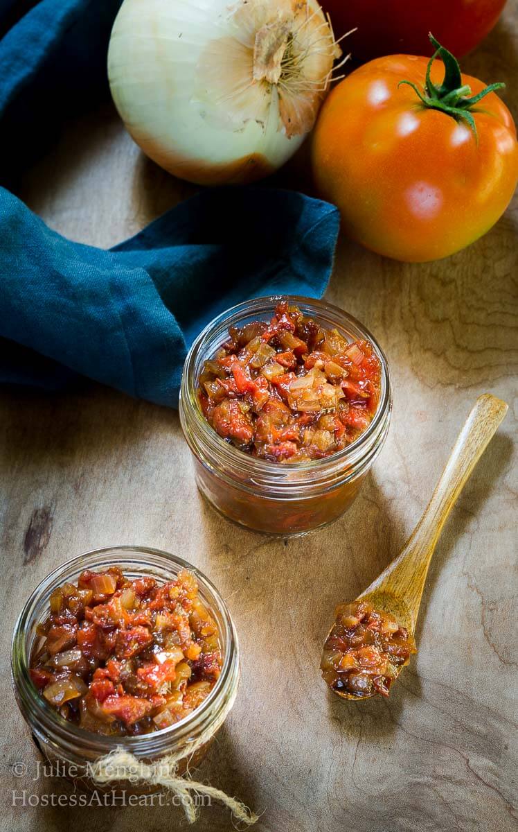 Top view looking into 2 jars of diced tomato onion chutney with a fresh onion and tomato sitting behind it.