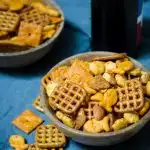 Side angle of two wooden bowls filled with Siracha Snack Mix sitting over a blue napkin.