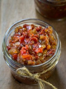 Top view of a jar of tomato onion chutney with a hemp string tied around it sitting on top of a wooden board.