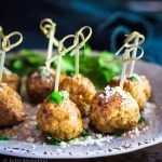 table view of 5 meatballs with wooden skewers sitting on a gray plate garnished with parsley and grated cheese in front of a blue napkin