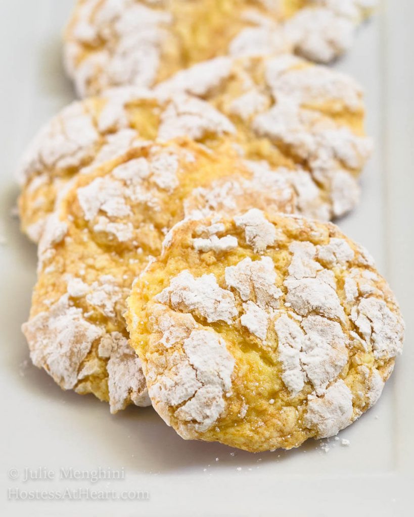 Front table view of yellow Lemon Snowflake cookies layered in a row on a white plate.