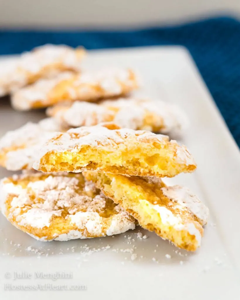 Yellow Lemon Snowflake cookies layered on a white plate with a broken cookie in the front showing the soft center. 