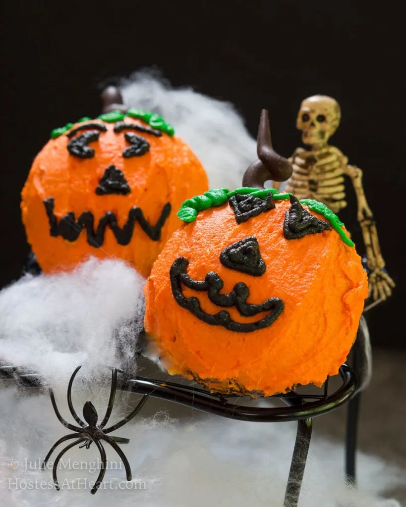 Photo of two pumpkin cakes with a skeleton, spider, and spider web in the background.