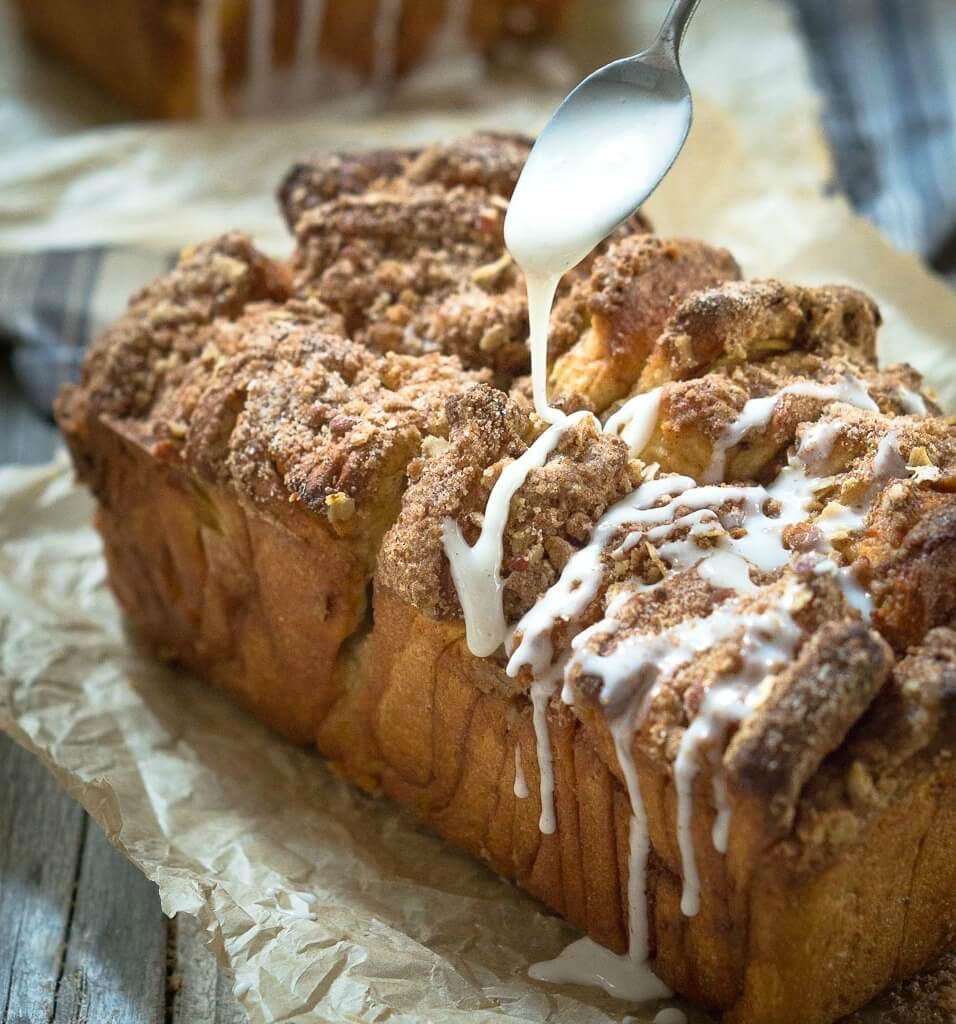 A loaf of Apple Pecan bread with a streusel top being drizzled with a white sugar glaze.
