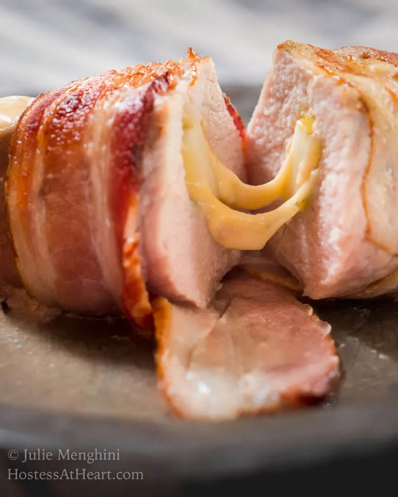 Sliced pork chop wrapped in bacon and filled with apple and melted cheese running through it.
