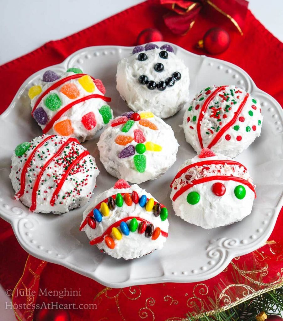 Cake balls frosted in white frosting decorated with candy pieces to resemble Christmas bulbs on a white snowflake plate sitting over a red napkin. 