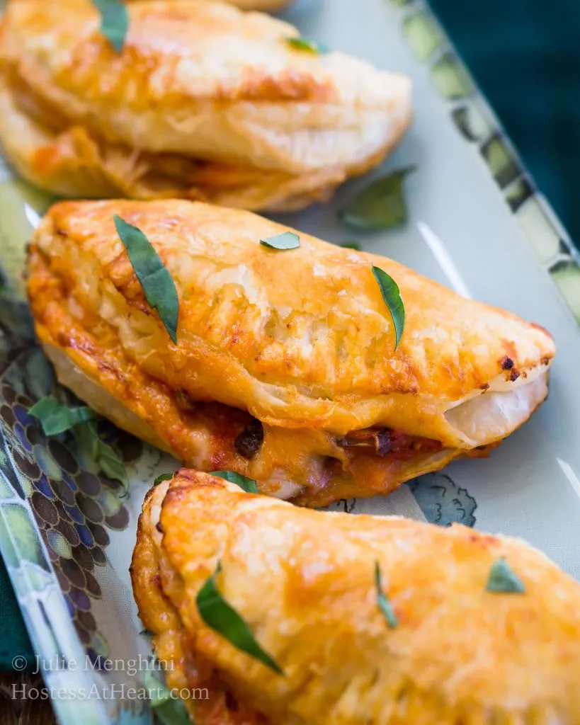 A tray of Cheese and Mushroom Empanadas garnished with grated cheese and fresh basil.