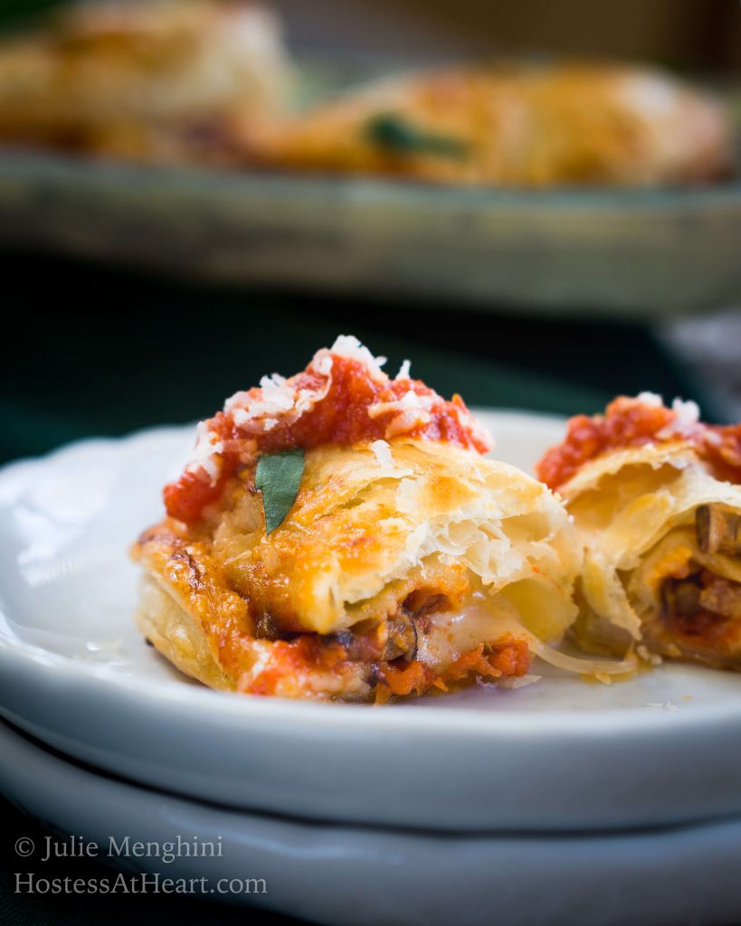 Front angle of a sliced-open cheese and mushroom empanada topped with a thick tomato marinara and grated cheese over a white plate.