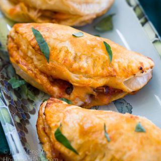 A close-up Cheese and Mushroom Empanadas sitting on a plate and garnished with fresh parsley.