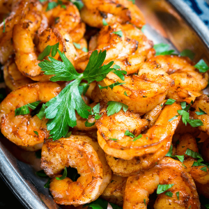 Close up top down view of shrimp seasoned in a red blackened seasoning and garnished with fresh parsley on a silver platter.