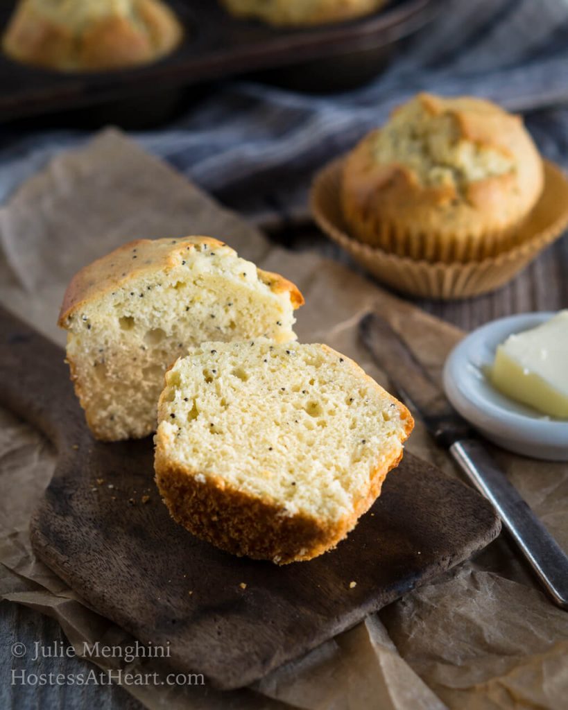 Muffin sliced in half with a pad of butter and a full muffin in the background.