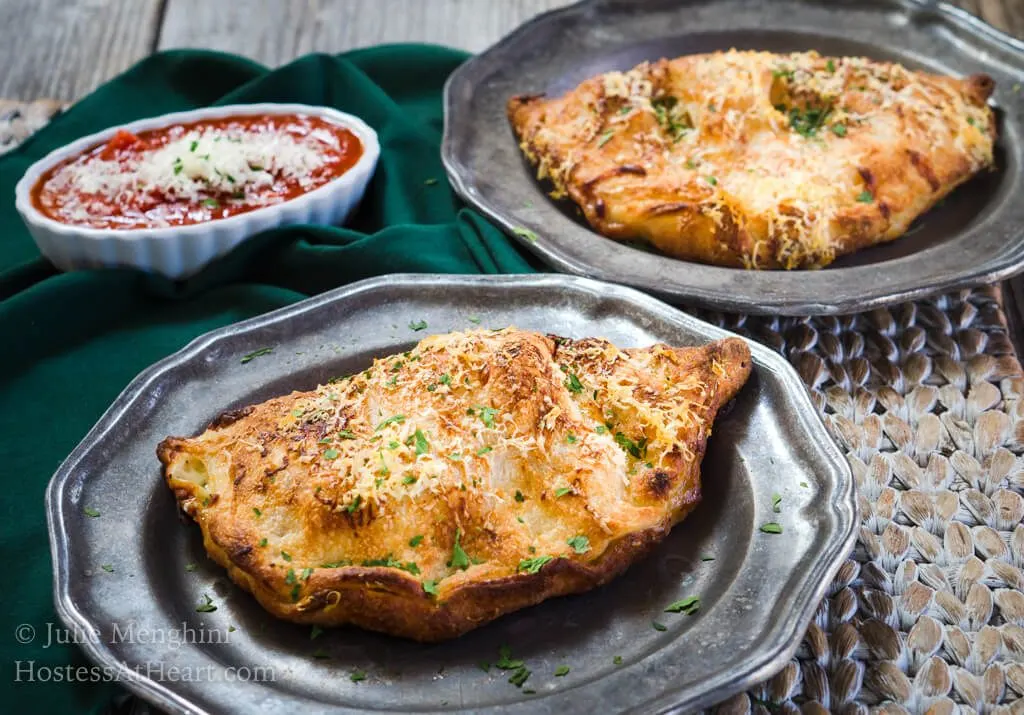 Ham and 3 Cheese Calzone sitting on a metal plate with a dish of marinara in the background 