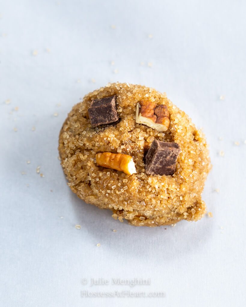 Raw cookie dough with chocolate pieces and pecans pressed into it.