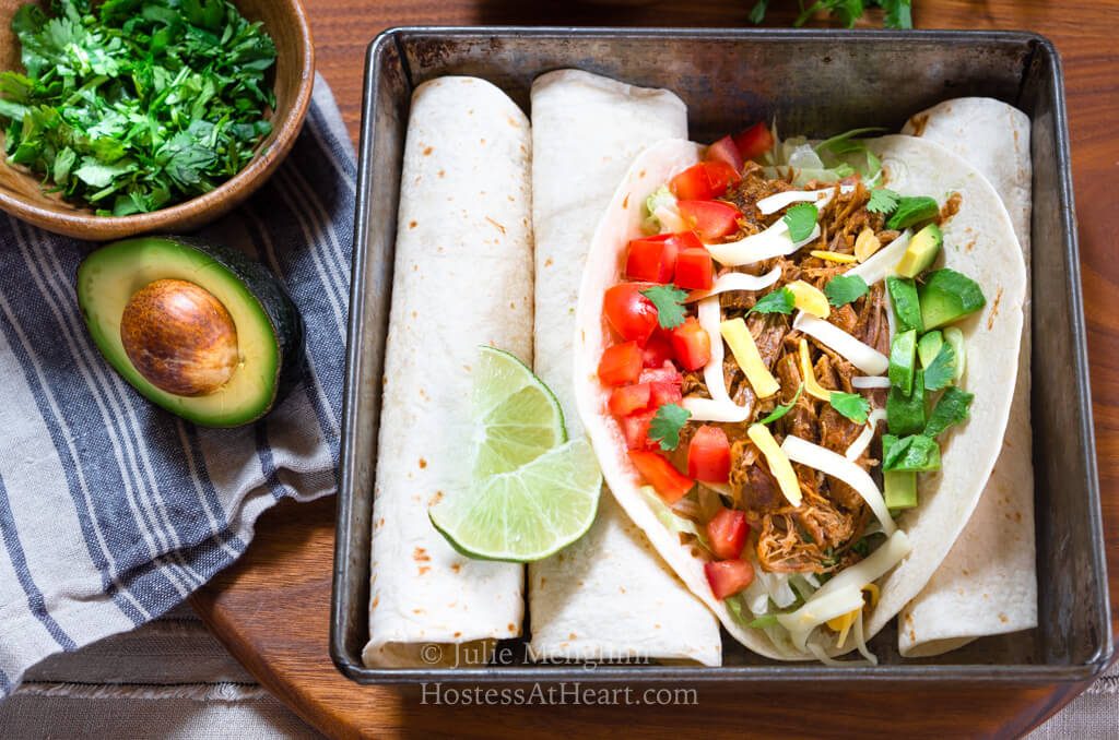 Horizontal shot of pork tacos with ingredients and extra tortilla shells