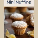 Sideview of a mini muffin dusted with powdered sugar surrounded by pieces of candied ginger Hostess At Heart