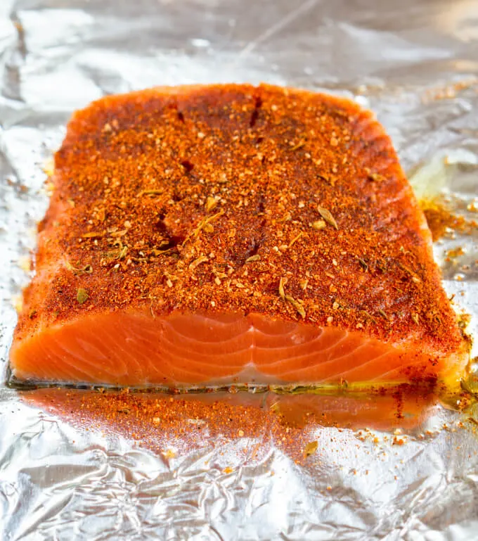 A top angle photo of a piece of raw salmon rubbed with blackened seasoning on a piece of foil.