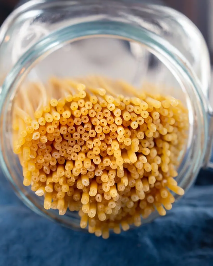 A jar filled with bucatini, a long tube shaped pasta with a whole through the center
