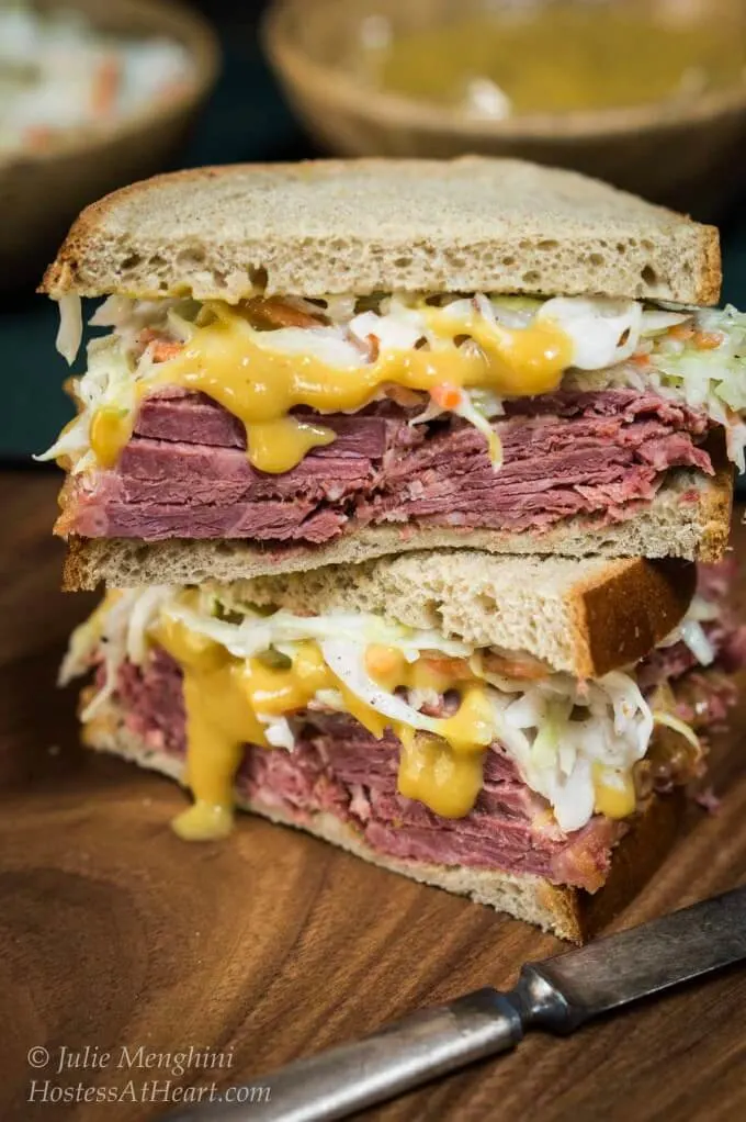 Thick half Corned Beef Cabbage Slaw Sandwich is layered with a mustard sauce. baked corned beef and a caraway slaw. The other half of the sandwich is stacked on top of the other half.