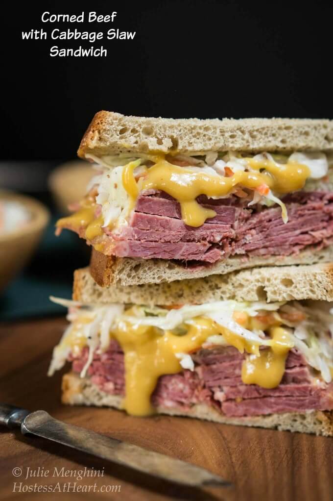 Stacked two halves of a corned beef sandwich with layers of brown sugar mustard and caraway slaw between to slices of rye bread.