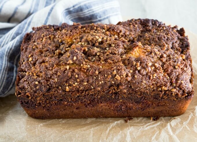 Table view of a loaf of Orange Pecan Streusel Coffee Cake with a thick brown sugar pecan streusel sitting horizontally on a piece of parchment paper.