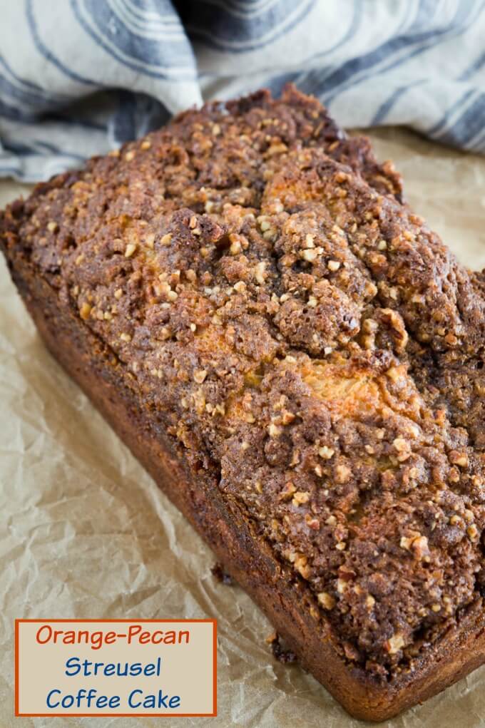 A loaf of Orange Pecan Streusel Coffee Cake with a thick brown sugar pecan streusel sitting at an angle on a piece of parchment paper.