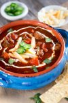 Chili Con Carne is a thick spicy stew loaded with meat and jalapenos. A pretty sour cream swirl and chopped cilantro mellows out the heat.