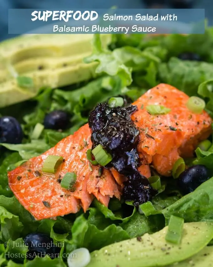 Green lettuce is adorned with a thick piece of salmon topped with a balsamic blueberry sauce. Sliced avocado sits in the background and the recipe title \"Salmon Salad with Balsamic Blueberry Sauce\" is printed across the top.