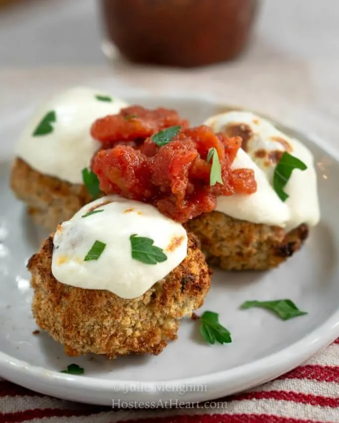 3 baked chicken parmesan meatballs topped with melted mozzarella and chunky marinara on a plate