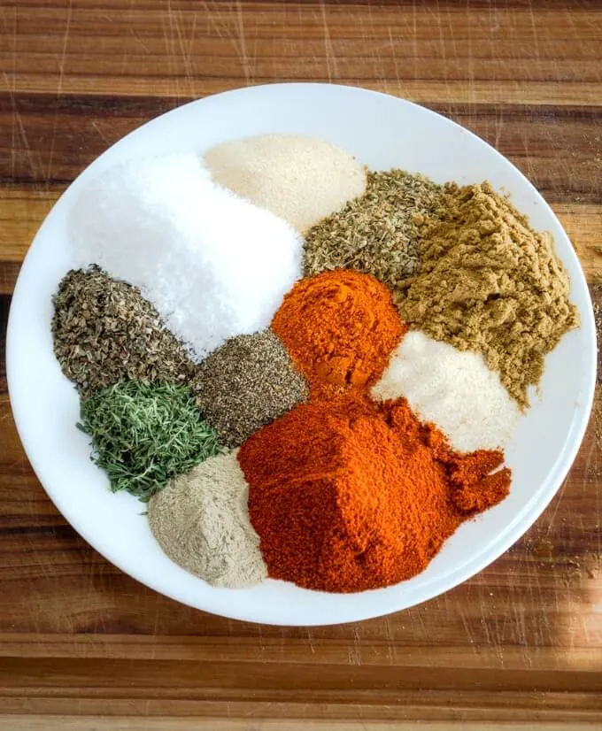 A white plate loaded with fresh spices and herbs that make a savory spicy Creole Seasoning blend.