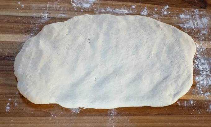 Ciabatta dough rolled flat on a wooden cutting board.