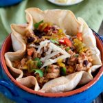 Green Chili Pork, corn, black beans and rice inside a tortilla bowl garnished with cheese
